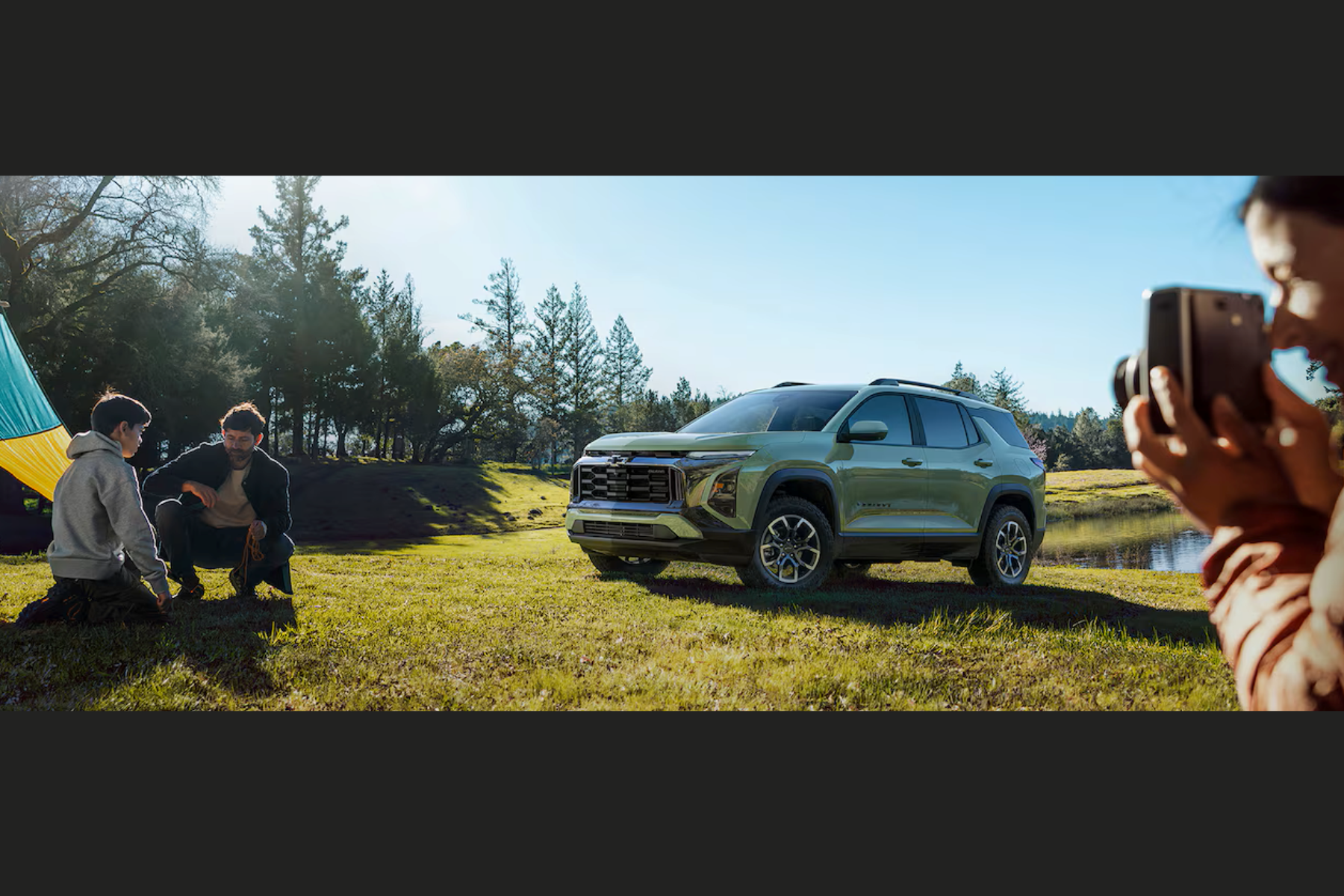 kids playing near a 2026 Chevy Equinox while parent takes a photo on their phone.